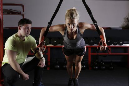 Kvinne som gjør styrkeøvelser med personlig trener ved siden av som veileder